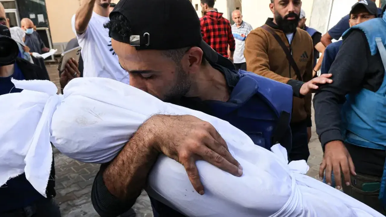 Salah satu warga di Gaza menggendong anaknya dalam balutan kain kafan yang tewas akibat perang antara Israel dan Hamas. (AFP/Mahmud Hams)