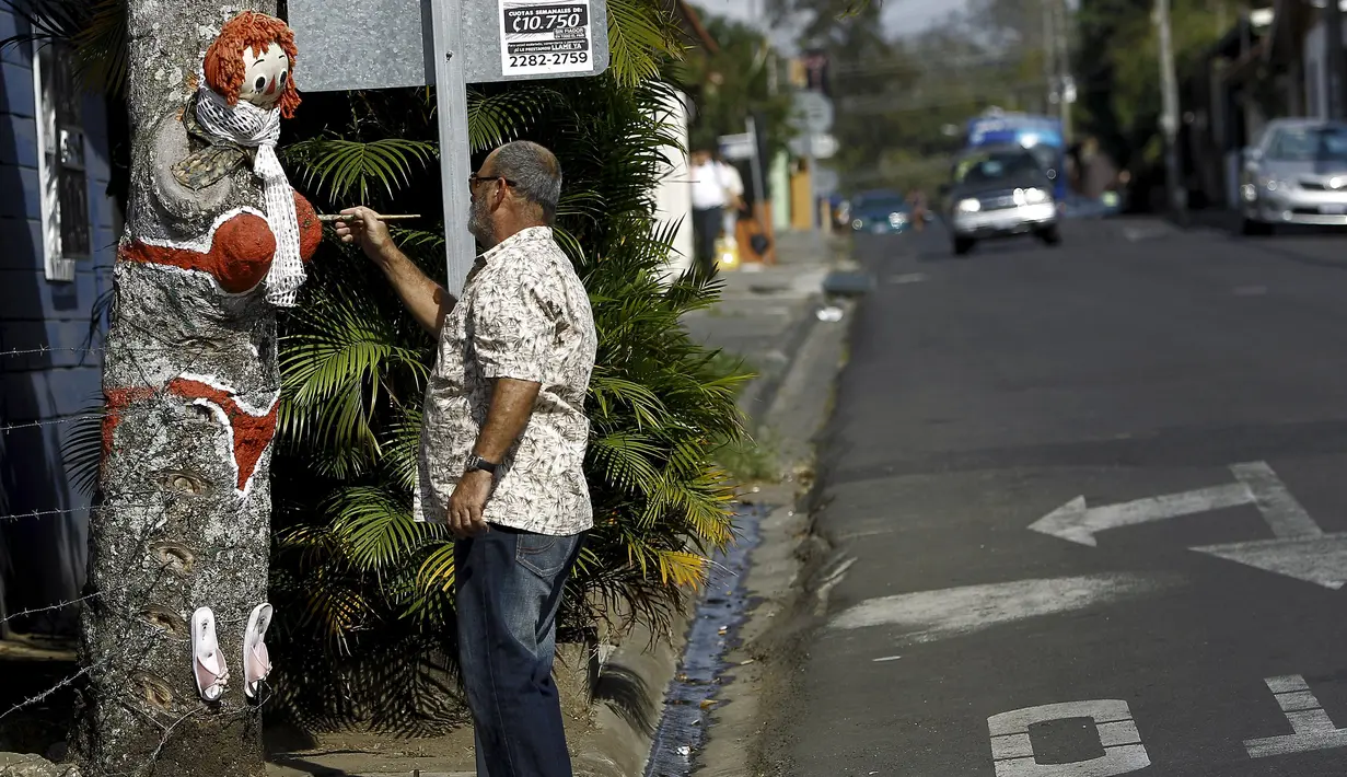 Gonzalo Sanchez melukis pohon mangga yang diberi nama "The Woman in Red Bikini", di sudut jalan di lingkungan Escazu, Kosta Rika, Selasa (1/3). Lukisan tersebut menirukan sosok seorang wanita yang mengenakan bikini. (REUTERS/Juan Carlos Ulate)