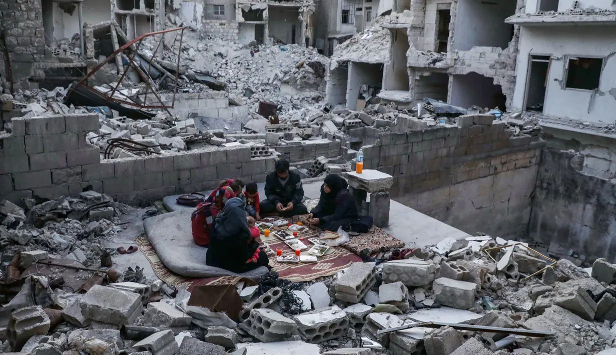Keluarga Tareq Abu Ziad menunggu waktu berbuka puasa di tengah reruntuhan rumah mereka yang hancur setelah serangan militer pasukan pemerintah dan sekutunya di Kota Ariha, Provinsi Idlib, Suriah, Senin (4/5/2020). Muslim Suriah melewati Ramadan tahun ini masih dalam kondisi perang. (AAREF WATAD/AFP)