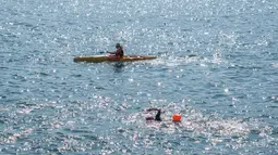 Seorang perenang (kanan) berenang melintasi Pelabuhan Victoria Hong Kong selama perlombaan renang lintas pelabuhan tahunan di Hong Kong, Minggu (12/12/2021). Namun, di bawah pembatasan covid-19 yang ketat, hanya setengah dari 3.000 perenang biasa yang diizinkan untuk berlomba. (Bertha WANG/AFP)