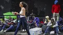 <p>Pejalan kaki melewati para migran yang menunggu dalam antrean di luar The Roosevelt Hotel yang digunakan oleh kota sebagai tempat tinggal sementara, Senin, 31 Juli 2023, di New York. (AP Photo/John Minchillo)</p>