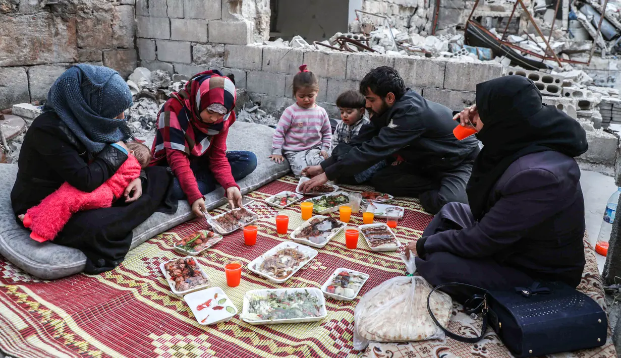 Keluarga Tareq Abu Ziad berbuka puasa di tengah reruntuhan rumah mereka yang hancur setelah serangan militer pasukan pemerintah dan sekutunya di Kota Ariha, Provinsi Idlib, Suriah, Senin (4/5/2020). Muslim Suriah melewati Ramadan tahun ini masih dalam kondisi perang. (AAREF WATAD/AFP)