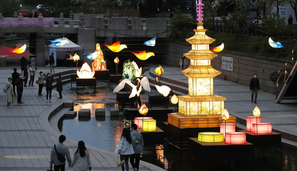 Pengunjung yang mengenakan masker wajah sebagai tindakan pencegahan penyebaran virus corona COVID-19 berjalan dekat lentera yang dipajang untuk perayaan ulang tahun Buddha pada 19 Mei mendatang di Seoul, Korea Selatan, Senin (10/5/2021). (AP Photo/Lee Jin-man)