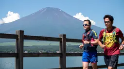 Dua pria jogging di Gunung Fuji, barat Tokyo, dengan latar belakang desa Yamanakako di prefektur Yamanashi pada 19 Juli 2021. Mendaki Gunung Fuji bukan hal yang mudah, tetapi pemandangan matahari terbit di atas lautan awan adalah hadiah terindah bagi yang mencapai puncak. (Charly TRIBALLEAU/AFP)