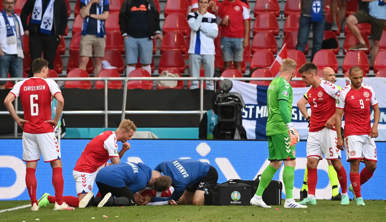 Petugas medis memeriksa gelandang timnas Denmark, Christian Eriksen setelah pingsan pada laga Denmark vs Finlandia di Grup B Euro 2020 di Parken Stadium, Copenhagen, Sabtu (12/6/2021). Laga dihentikan jelang berakhirnya babak pertama setelah Christian Eriksen pingsan. (NACKSTRAND/POOL/AFP)