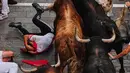 Seorang pengunjung festival terjatuh di depan banteng-banteng aduan Victoriano del Río saat acara lari banteng ketiga di festival San Fermín di Pamplona, Spanyol, Kamis, 9 Juli 2026. (AP Photo/Miguel Oses)