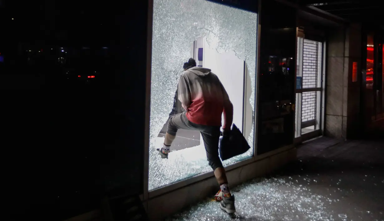 Seorang pendemo memasuki toko melalui jendela yang rusak di New York, AS (1/6/2020). Sejumlah toko di Amerika Serikat dijarah oleh pendemo yhang mengecam kematian warga kulit hitam George Floyd. (Foto AP / Frank Franklin II)