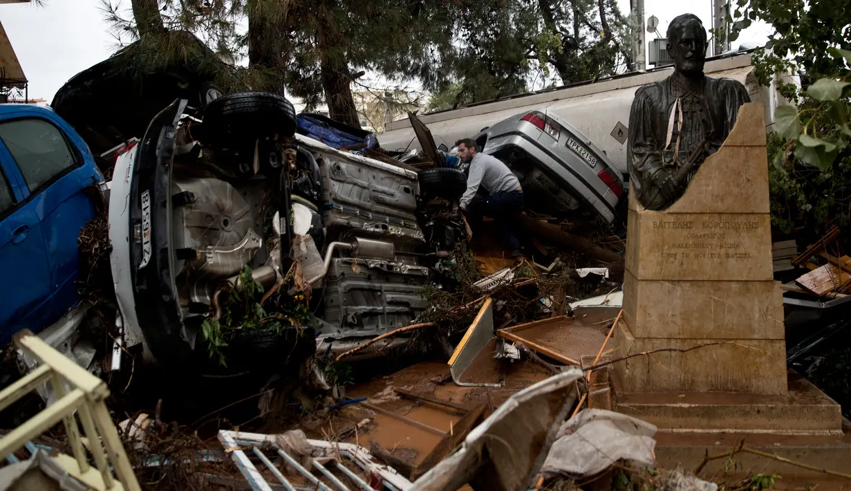Seorang pemilik mobil mengamati tumpukan kendaraan yang ringsek akibat diterjang banjir bandang di kota industri Mandra, barat Athena, Yunani, Rabu (15/11). Hujan lebat mengguyur sejumlah wilayah di Yunani sejak Selasa (14/11). (AP/Petros Giannakouris)