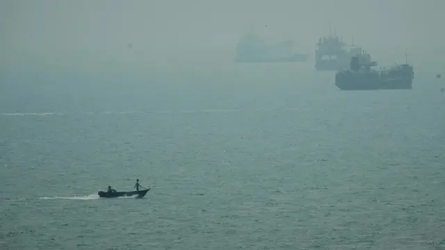 Sebuah perahu motor melintas di dekat kapal-kapal komersial yang berlabuh di tengah kabut di Selat Hormuz, lepas pantai Bandar Abbas, Iran, Senin (7/9/2026).