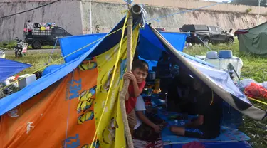 Seorang anak laki-laki mengintip dari tenda ketika orang-orang yang terkena gempa tinggal di kamp sementara setelah gempa berkekuatan 6,2 di Mamuju, Senin (18/1/2021). Ratusan jiwa telah mengungsi di sejumlah posko pengungsian karena rumah mereka rusak akibat gempa. (AFP/Adek Berry)