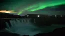 Langit berhias aurora borealis atau Cahaya Utara terlihat di atas air terjun Godafoss di Thingeyjarsveit, Islandia, 14 Oktober 2018. Lukisan abstrak alam semesta dari tabrakan spektrum warna Aurora Borealis begitu spektakuler. (Mariana SUAREZ/AFP)