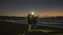 Dua wanita berfoto saat mereka menunggu matahari terbit di Pantai Selatan Chigasaki pada Hari Tahun Baru di Prefektur Kanagawa, barat daya Tokyo (1/1/2021). (AFP/Philip Fong)