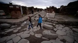 Wisatawan menyeberangi Via di Nola yang berbatu, Pompeii, Italia, Senin (25/11/2019). Kota Pompeii ditemukan 1.500 tahun setelah letusan gunung berapi Vesuvius yang tragis. (Filippo MONTEFORTE/AFP)