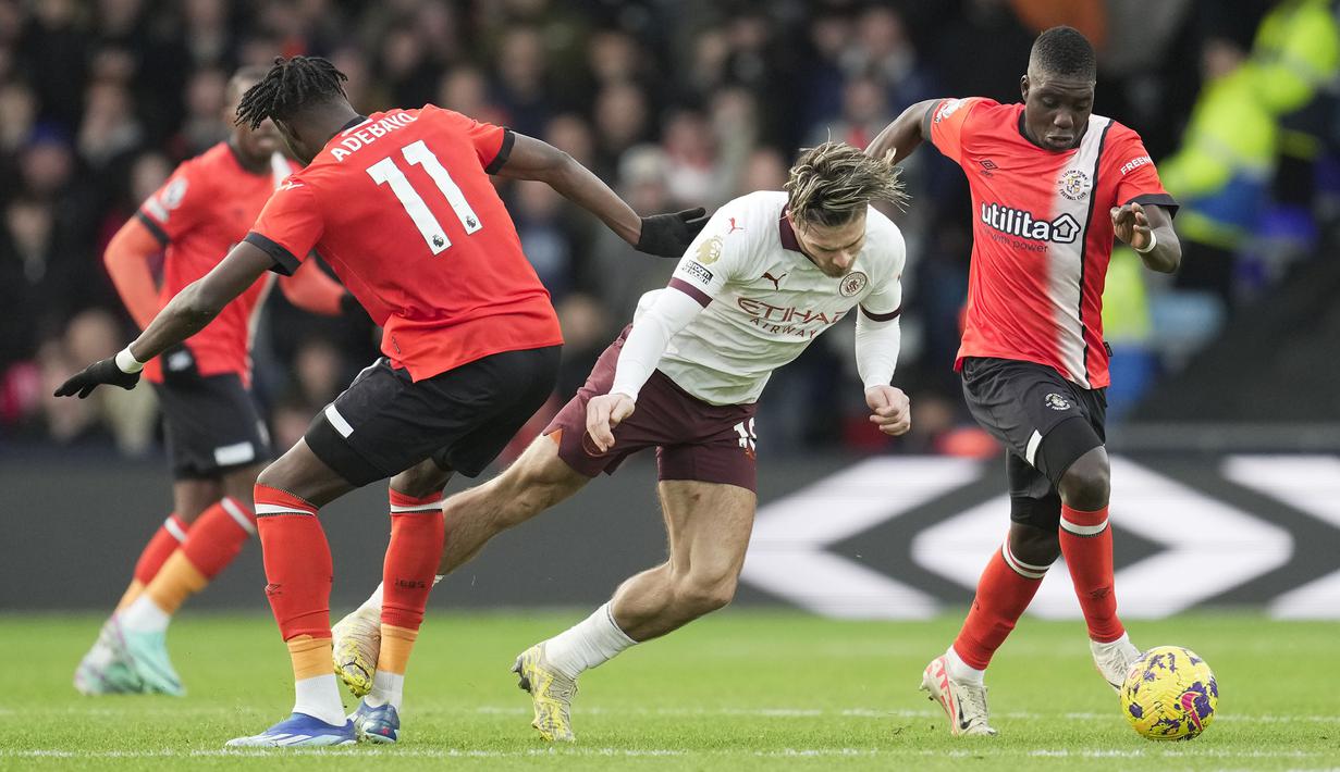 Gelandang Manchester City, Jack Grealish (tengah) ditekel striker Luton Town, Elijah Adebayo pada laga pekan ke-16 Liga Inggris 2023/2024 di Kenilworth Road, Luton, Minggu (10/12/2023) malam WIB. (AP Photo/Kin Cheung)