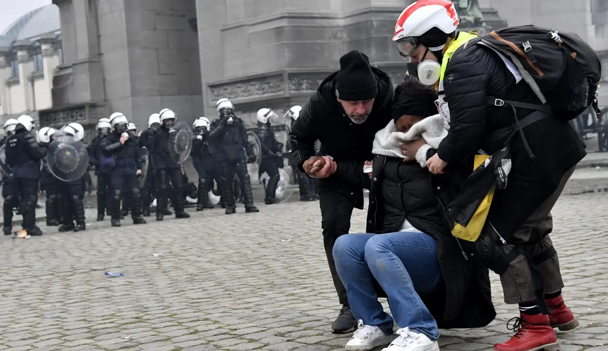 Dua orang membantu wanita yang terkena gas air mata saat demonstrasi menentang tindakan COVID-19 di Brussels, Belgia, Minggu (23/1/2022). Pengunjuk rasa juga mengkritik kebijakan wajib vaksin untuk beraktivitas di tempat umum maupun mengikuti kegiatan tertentu. (AP Photo/Geert Vanden Wijngaert)
