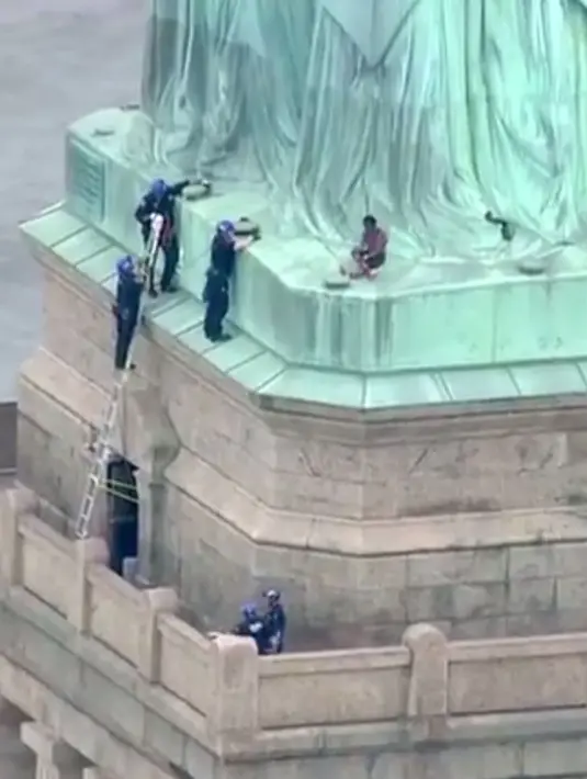 Petugas kepolisian membujuk seorang wanita yang memanjat Patung Liberty di New York, Rabu (4/7). Aksi yang digelar bersamaan dengan Hari Kemerdekaan AS tersebut dilakukan sebagai bentuk protes penanganan imigran oleh pemerintah AS. (AFP/PIX11 News/HO)