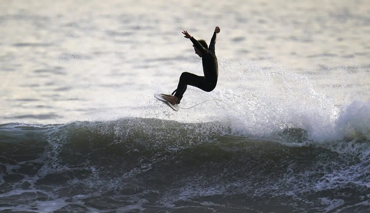 Seorang peselancar mengendarai ombak di Huntington Beach, California, Amerika Serikat, 12 Januari 2022. Peselancar di seluruh California Selatan berbondong-bondong ke daerah pantai saat gelombang ombak besar memasuki wilayah tersebut. (AP Photo/Ashley Landis)