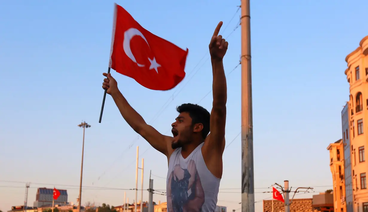 Seorang pria mengibarkan  bendera nasional Turki di Taksim Square, pusat kota Istanbul, Sabtu (16/7). Ratusan warga turun ke jalan merayakan kegagalan kudeta militer di Turki terhadap Pemerintahan Erdogan. (REUTERS/Kemal Aslan)