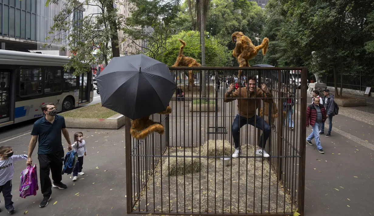 <p>Seorang pengunjung menirukan hewan yang dikurung saat memanjat instalasi seni karya seniman Brasil Eduardo Srur di sepanjang Paulista Avenue, Sao Paulo, Brasil, 6 Mei 2022. Menurut Eduardo Srur, pameran "Vida Livre" atau "Kehidupan Bebas" bertujuan memprovokasi masyarakat agar memikirkan kembali budaya hewan yang terperangkap untuk hiburan manusia. (AP Photo/Andre Penner)</p>