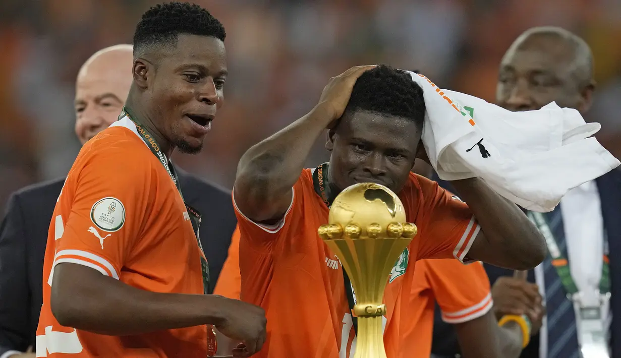 Ekspresi bahagia pemain Pantai Gading, Karim Konate (kanan) saat berdiri di samping trofi setelah laga final Piala Afrika 2023 melawan Nigeria di Alassane Ouattara Olympic Stadium, Ebimpe, Abidjan, Pantai Gading, Minggu (11/02/2024) waktu setempat. (AP Photo/Themba Hadebe)