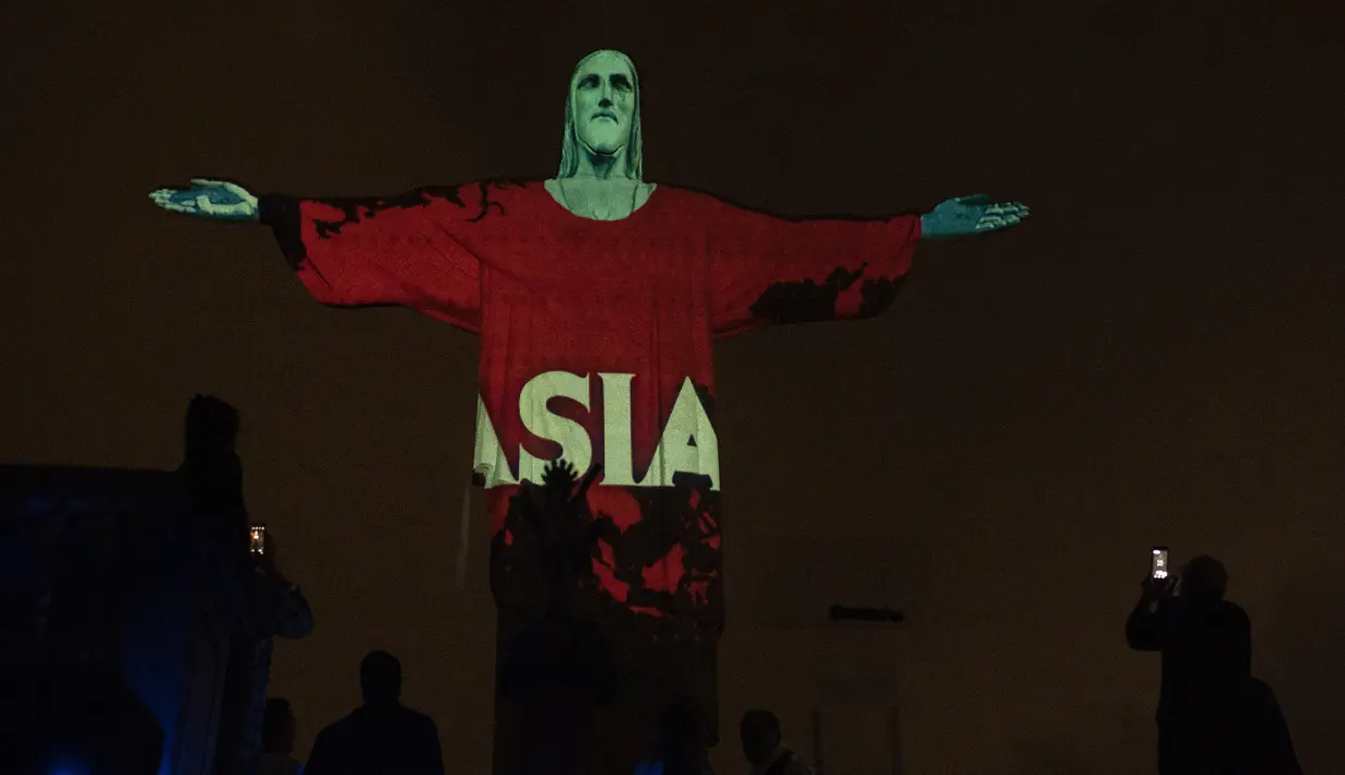 Patung Christ the Redeemer bermandi cahaya dengan peta dan kata ‘Asia’ di Rio de Janeiro, Brasil, Rabu (18/3/2020). Pertunjukan ini untuk menunjukkan dukungan bagi mereka yang menderita virus corona COVID-19. (AP Photo/Silvia Izquierdo)