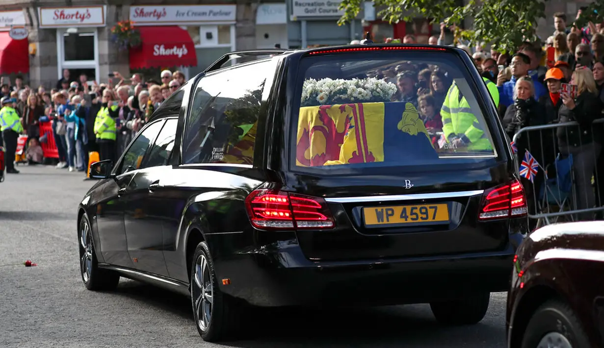 Warga berbaris saat mobil yang membawa peti berisi jenazah Ratu Elizabeth II melintas di Ballater, Skotlandia, Minggu (11/9/2022). Jenazah Ratu Elizabeth II diberangkatkan dari Kastil Balmoral ke Istana Holyroodhouse di Edinburgh sebelum nantinya akan dipindahkan ke London. (AP Photo/Scott Heppell)