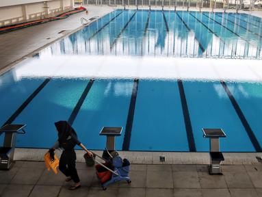 Petugas kebersihan berjalan dekat kolam Stadion Akuatik Gelora Bung Karno (GBK), Jakarta, Rabu (11/7). Stadion ini memiliki 3 kolam utama dan 1 kolam pemanasan berstandar Olimpiade dari FINA (Federasi Renang Internasional). (Liputan6.com/Faizal Fanani)