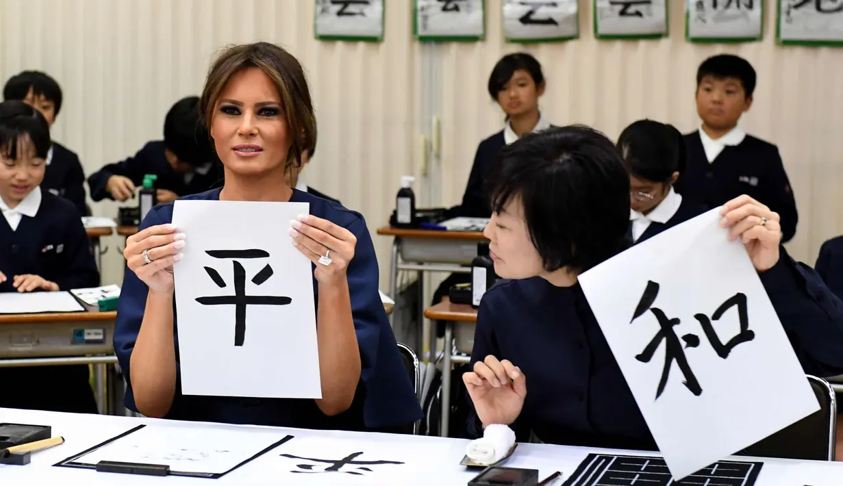 Melania Trump (kiri) dan Istri PM Jepang, Akie Abe menunjukkan huruf kanji yang berarti "Damai" saat menghadiri kelas kaligrafi di sekolah dasar Kyobashi Tsukiji, Tokyo (6/11). (AFP Photo/Pool/Toshifumi Kitamura)