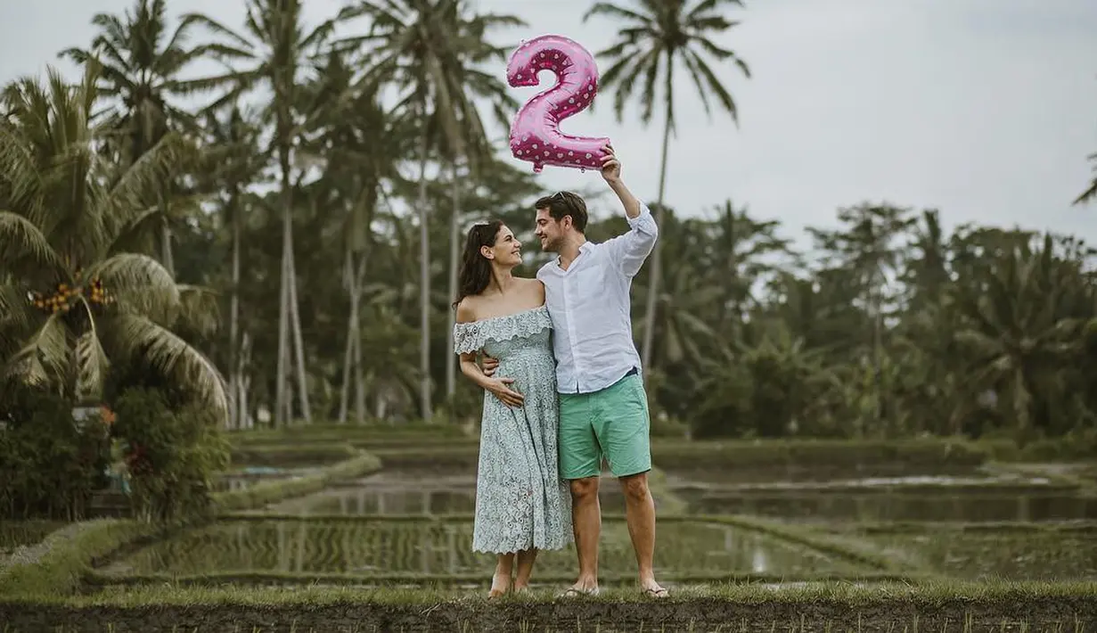 Berdiri di persawahan, Marissa dan suaminya, tampak mesra. Tampilan Marissa juga begitu cantik dengan dress model off-shoulders yang bermotif bunga-bunga ini. (Instagram/marissaln)