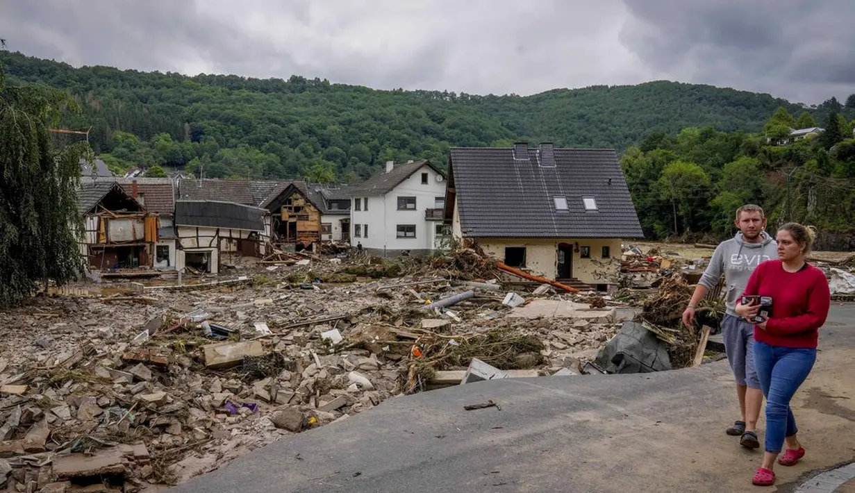Sepasang suami istri berjalan melewati rumah-rumah yang hancur di Schuld, Jerman, Kamis (15/7/2021). Korban banjir di Jerman barat bertambah menjadi setidaknya 58 orang per Kamis malam (15/7) waktu setempat.(AP Photo/Michael Probst)