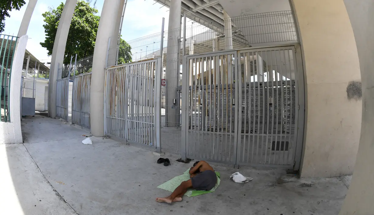 Seorang tunawisma tidur di luar gerbang utama Stadion Maracana, Brasil (18/1). Hanya berselang lima bulan usai menjadi ikon Olimpiade 2016, kondisi terbaru Stadion Maracana tampak tak terurus. (AFP PHOTO / Vanderlei Almeida)