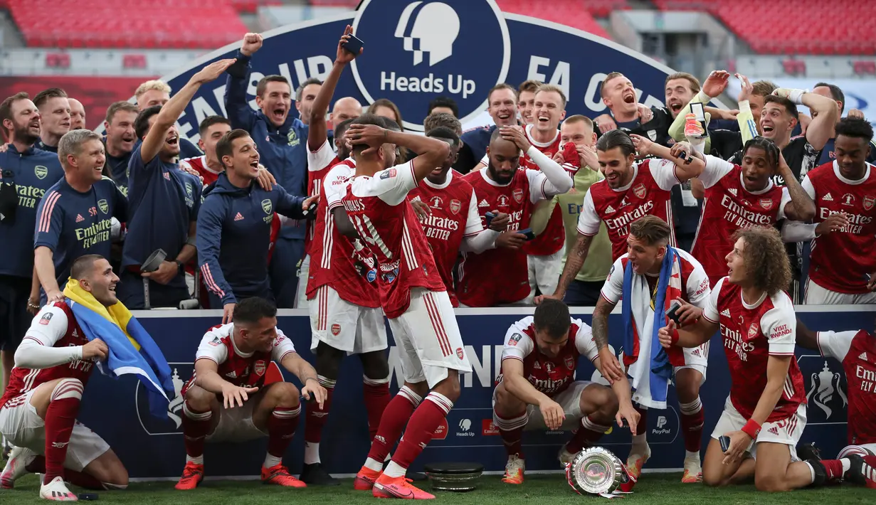 Striker Arsenal, Pierre-Emerick Aubameyang (tengah) menjatuhkan trofi saat merayakan gelar juara Piala FA usai mengalahkan Chelsea pada pertandingan final Piala FA di stadion Wembley, Minggu (2/8/2020).  Aubameyang terlihat kaget sambil memegang kepalanya saat trofi terjatuh. (Adam Davy/Pool via AP)