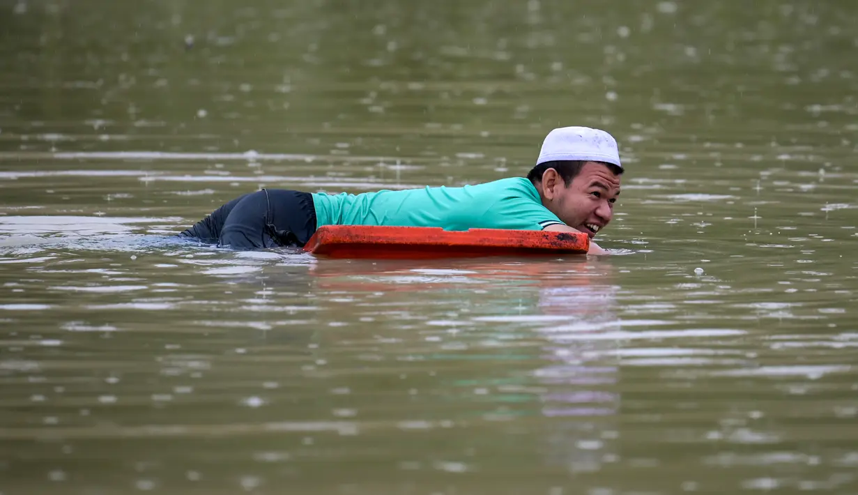 Seorang penduduk menggunakan penutup sebagai alat pelampung saat dia berenang di air banjir di Lanchang di negara bagian Pahang Malaysia (6/1/2021). (AFP/Mohd Rasfan)