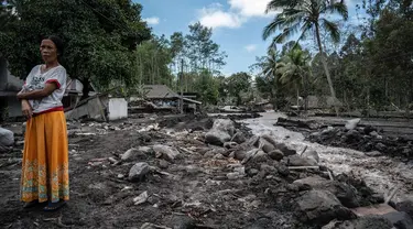 Seorang wanita berdiri dekat rumah yang rusak di Dusun Kamar Kajang, Lumajang, Kamis (9/12/2021). Puluhan rumah di dusun tersebut terendam luapan air sungai bercampur material lahar dingin erupsi Gunung Semeru akibat diguyur hujan deras pada Selasa (7/12) dan Rabu (8/12) malam. (Juni Kriswanto/AFP)