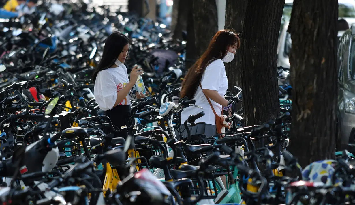Dua orang wanita berjalan melintasi sepeda-sepeda yang diparkir memenuhi trotoar di Beijing, China (21/7/2020). Selama dua tahun terakhir, Pemerintah Beijing telah menyediakan fasilitas persewaan sepeda menggunakan sistem bike sharing. (AFP Photo/Greg Baker)