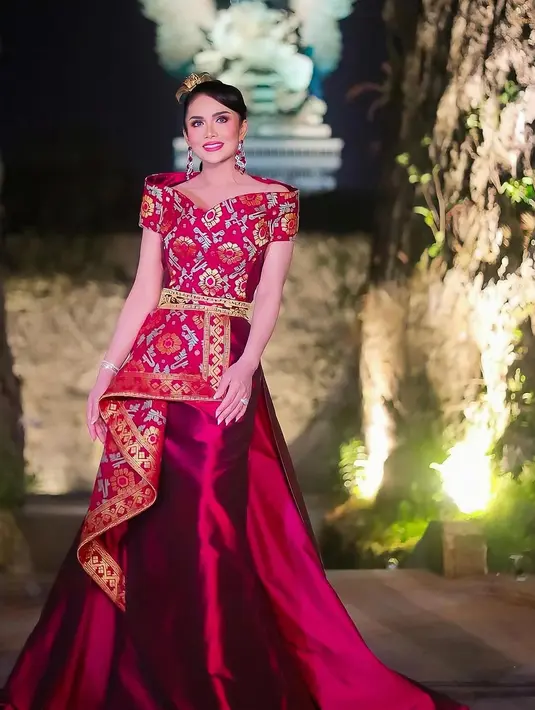 Krisdayanti tampak memukau dengan gaun panjang berwarna ungu tua yang dipadukan dengan motif khas Bali yang dominan di bagian atasan. Hiasan kepala sederhana namun anggun menambah daya tariknya. [@mamauthe/@3divaofficial].