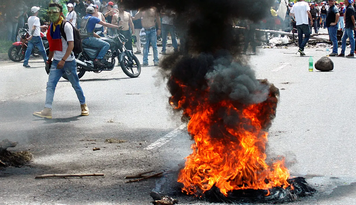 Seorang demonstran berjalan di dekat ban yang dibakar saat aksi unjuk rasa anti-Presiden Nicolas Maduro di San Cristobal, Venezuela, (26/10). Sekitar 120 orang terluka dan 147 demonstran lainnya ditangkap polisi. (REUTERS/Carlos Eduardo Ramirez)