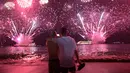 Dua pria berangkulan saat menyaksikan pesta kembang api menyambut Tahun Baru 2019 di Pantai Copacabana, Rio de Janeiro, Brasil, Selasa (1/1). (AP Photo/Leo Correa)