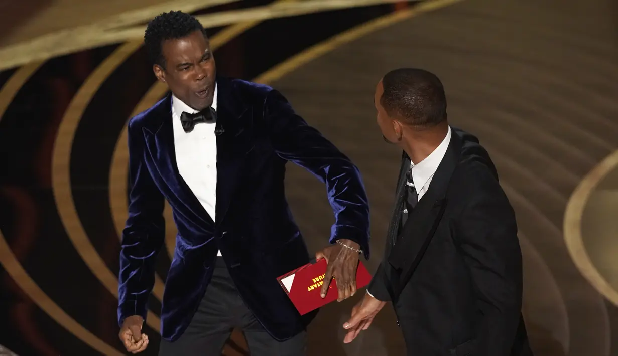 Reaksi presenter Chris Rock setelah dipukul oleh Will Smith di atas panggung Piala Oscar 2022 saat penghargaan untuk film dokumenter terbaik di Dolby Theatre, Minggu (27/3/2022). Will Smith merasa lawakan sang komedian terkait istrinya, Jada Pinkett Smith keterlaluan. (AP Photo/Chris Pizzello)