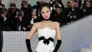 Dalam debutnya di Met Gala 2023, Jennie memakai outfit gaun mini putih satin dengan detail pita dan bunga Kamelia. Gaun rilisan Chanel koleksi Fall 1990 itu dipadukan dengan stocking dan heels. Ia juga memakai gloves dan choker hitam sebagai penyempurna tampilan. [@themetgalaofficial]