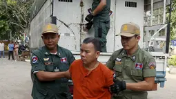 Yem Chrin (tengah) dikawal oleh petugas polisi saat tiba di Pengadilan Provinsi Battambang,Kamboja,Kamis (3/12). Diduga dalam prakteknya Yem Chrin menggunakan obat tak berlisensi, suntik bekas dan melakukan malpraktek. (REUTERS/Stringer)