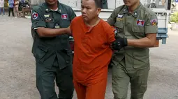 Yem Chrin (tengah) dikawal oleh petugas polisi saat tiba di Pengadilan Provinsi Battambang,Kamboja,Kamis (3/12). Diduga dalam prakteknya Yem Chrin menggunakan obat tak berlisensi, suntik bekas dan melakukan malpraktek. (REUTERS/Stringer)