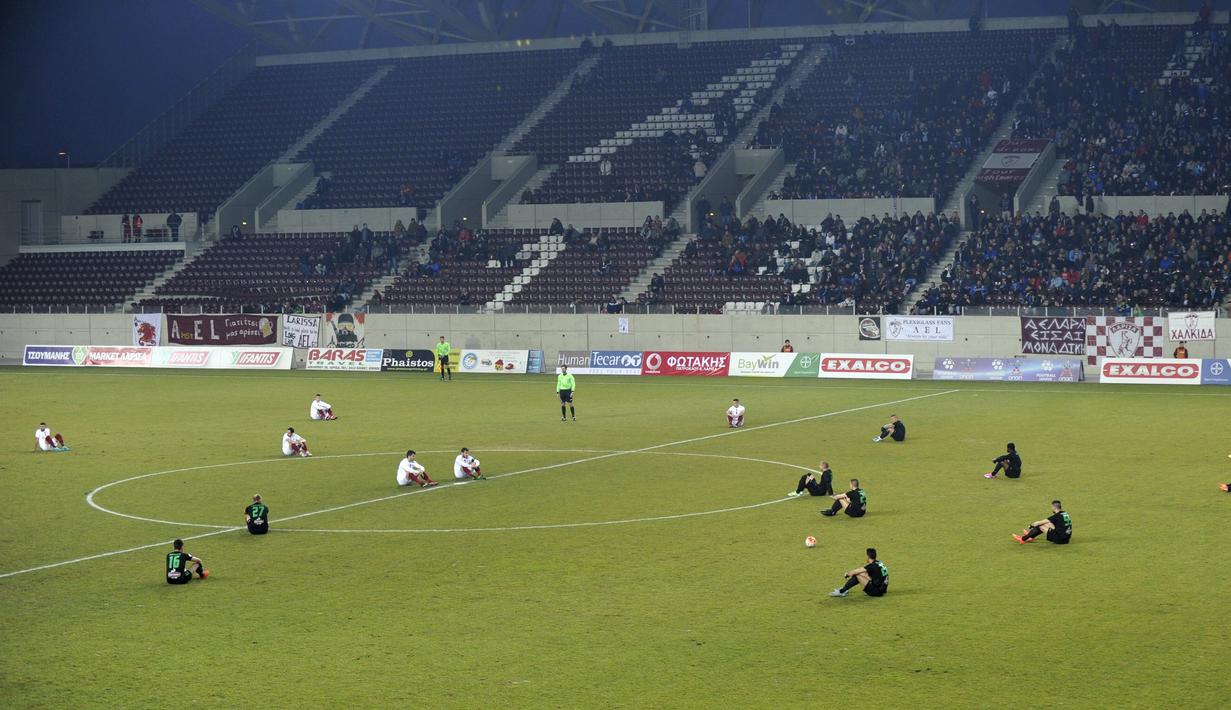 Pemain AEL Larissa dan Acharnaikos duduk di lapangan sebagai bentuk penghormatan kepada para migran yang meninggal dunia di Pulau Aegea sebelum memulai pertandingan di Larisa, Yunani, (29/1/2016). (Reuters/Kostas Tsomakos)