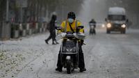Orang-orang bepergian melintasi jalan saat salju turun di Beijing, China, Minggu (7/11/2021). Badai salju awal musim telah menyelimuti sebagian besar Cina utara termasuk ibu kota