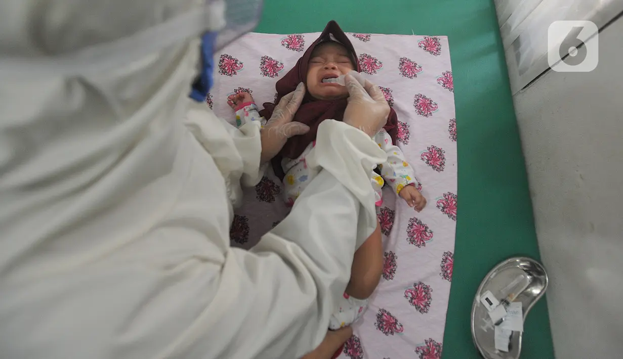 Dokter dengan Alat Pelindung Diri memberikan vaksin polio pada anak di Rumah Vaksinasi Sawangan, Depok, Selasa (16/6/2020). Orang tua diminta tidak menunda pemberian imunisasi pada anak-anak yang masih harus menerima imunisasi lengkap, meskipun Covid-19 belum berakhir. (merdeka.com/Arie Basuki)