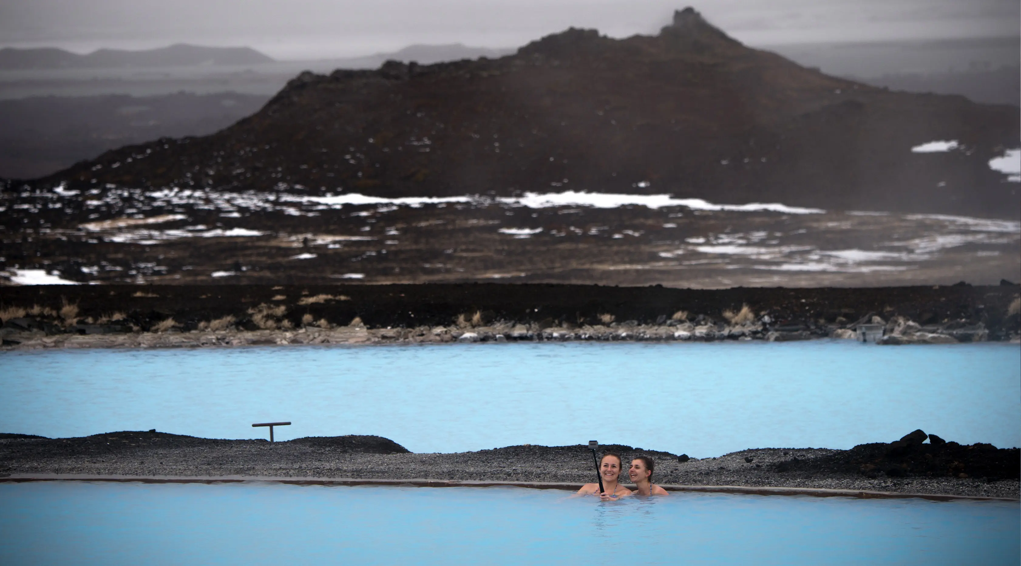 Dua wanita berselfie saat mereka berenang di sumber air panas di Myvatn, Islandia (12/4). Myvatn adalah danau eutrophic dangkal yang terletak di daerah vulkanisme aktif di utara Islandia, tidak jauh dari gunung berapi Krafla. (AFP Photo/Loic Venance)