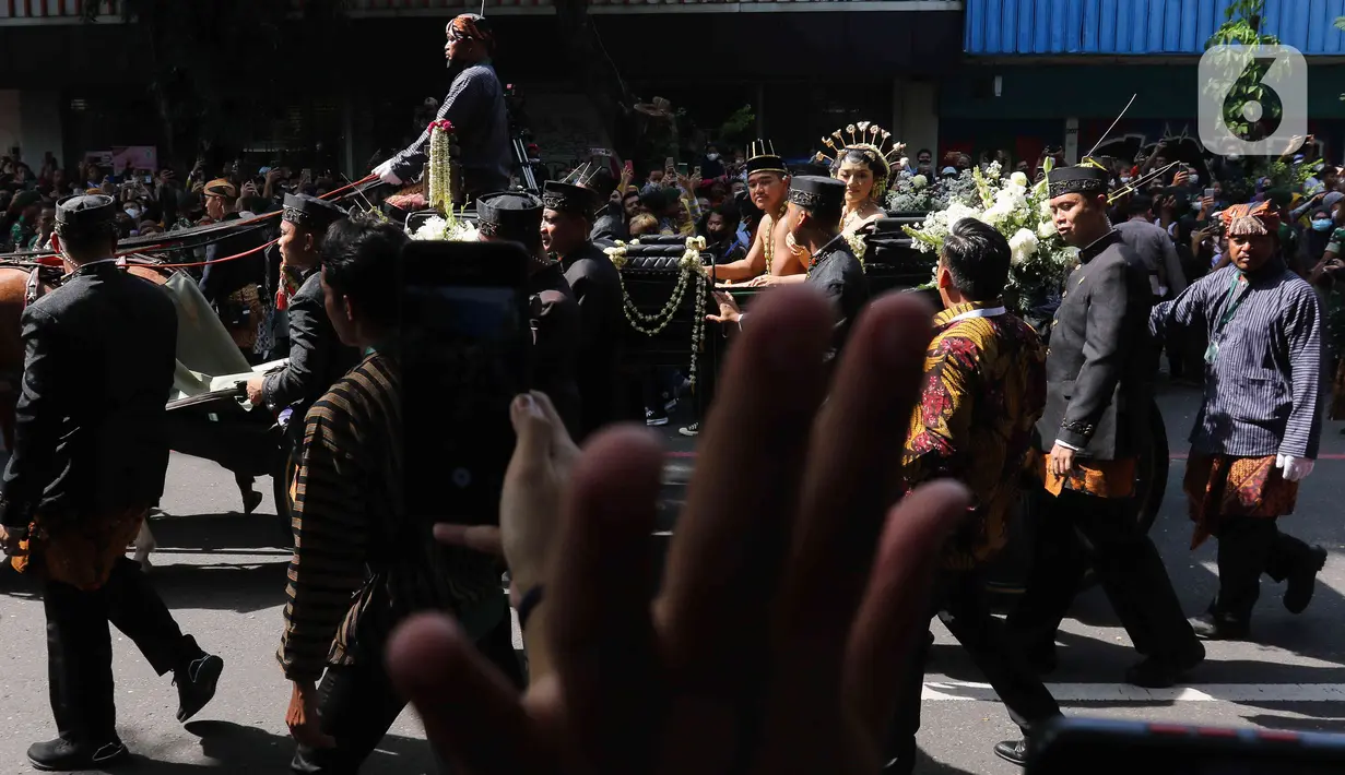 Pasangan pengantin Kaesang Pangarep dan Erina Gudono menaiki kereta saat prosesi kirab Ngunduh Mantu di kawasan Selamet Riyadi, Solo, Jawa Tengah, Minggu (11/12/2022). Kirab ngunduh mantu pernikahan putra bungsu Presiden Joko Widodo, Kaesang Pangarep dan istrinya Erina Gudono yang dimulai dari Loji Gandrung menuju Pura Mangkunegaran tersebut disaksikan ribuan masyarakat Solo dan sekitarnya. (Liputan6.com/Herman Zakharia)