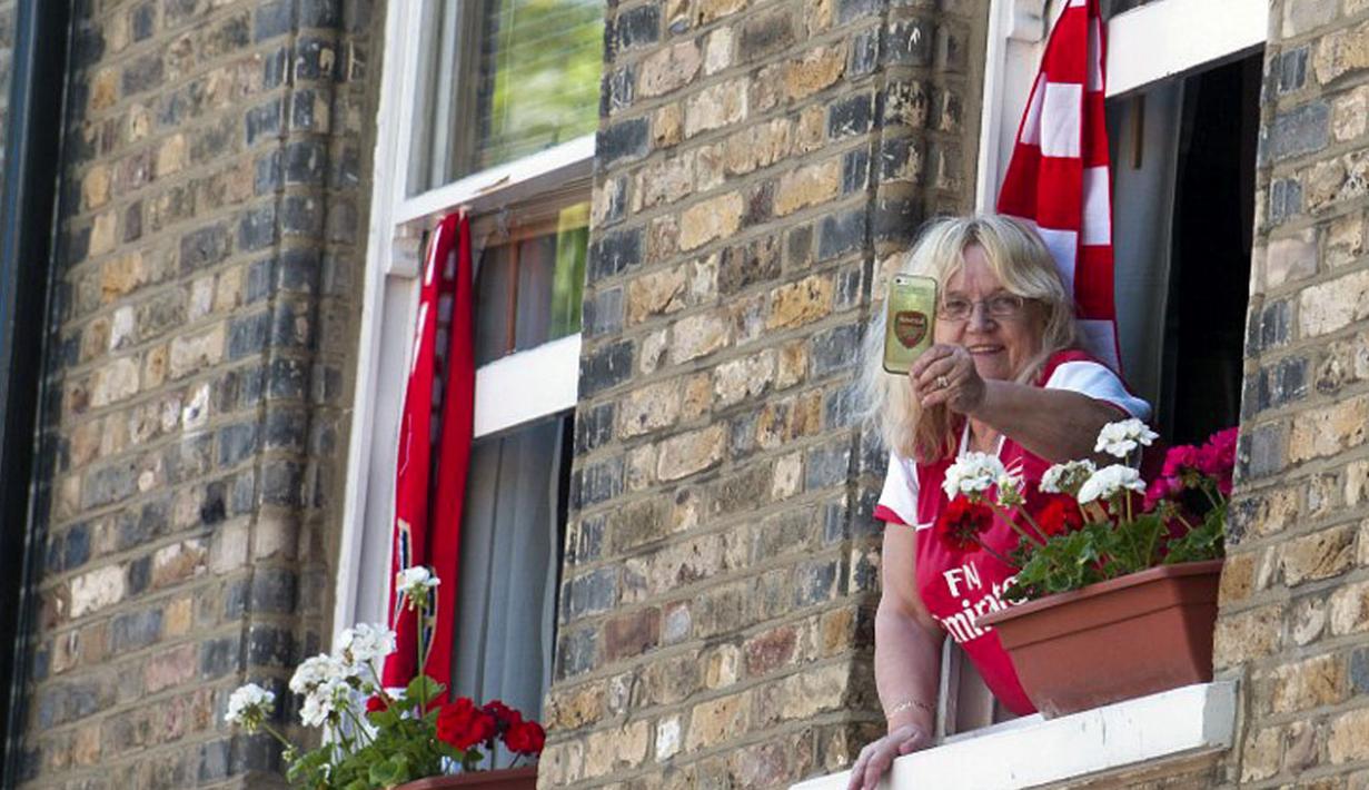 Dari balik jendela, salah satu suporter Arsenal berusaha mengabadikan parade kemenangan  "The Gunners" di London, Inggris, (18/5/2014). (AFP PHOTO/Oliver Will)