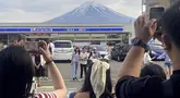 Para pengunjung mengambil foto di depan toko serba ada di kota Fujikawaguchiko, prefektur Yamanashi, Jepang, dengan latar belakang Gunung Fuji pada tanggal 28 April 2024. (Kyodo News via AP)