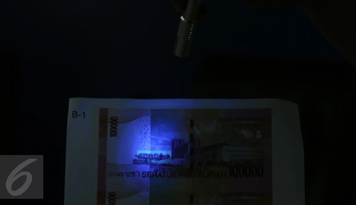 Petugas memperlihatkan uang palsu yang lolos sensor UV saat rilis di Bareskrim Mabes Polri, Gedung KKP, Jakarta, Senin (10/10). Peredaran dikendalikan dari rutan, empat tersangka diamankan dalam kasus ini. (Liputan6.com/Helmi Fithriansyah) 